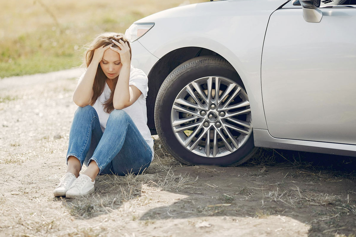 Frustrated woman sitting by a car with a flat tire.